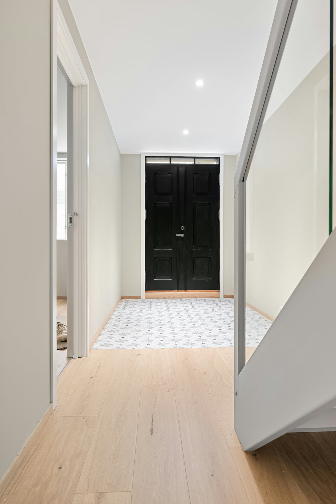 A white hallway with a black door and a wooden floor