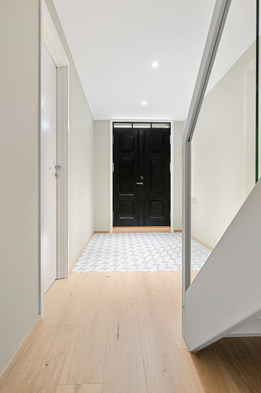 A white hallway with a black door and a wooden floor