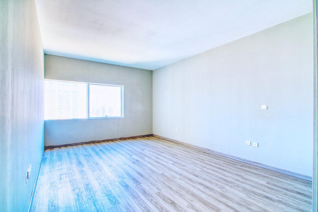 An empty room with a window and wood floor.