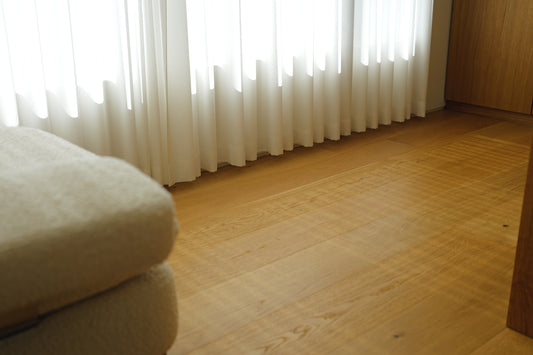 A bed and wooden floor near a window with curtains